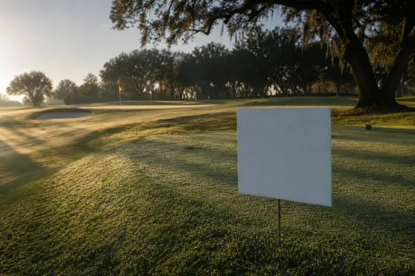 A blank sponsor sign beside a tee box at dawn